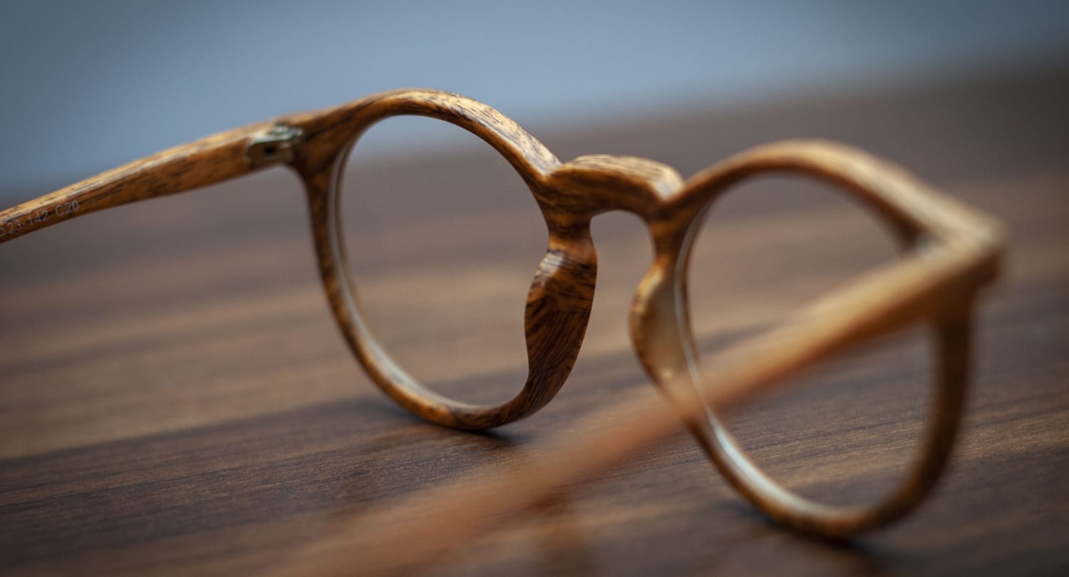 Close-up of eco-friendly wooden eyeglass frames on a wooden surface, symbolizing sustainable eyewear choices for eco-conscious consumers.